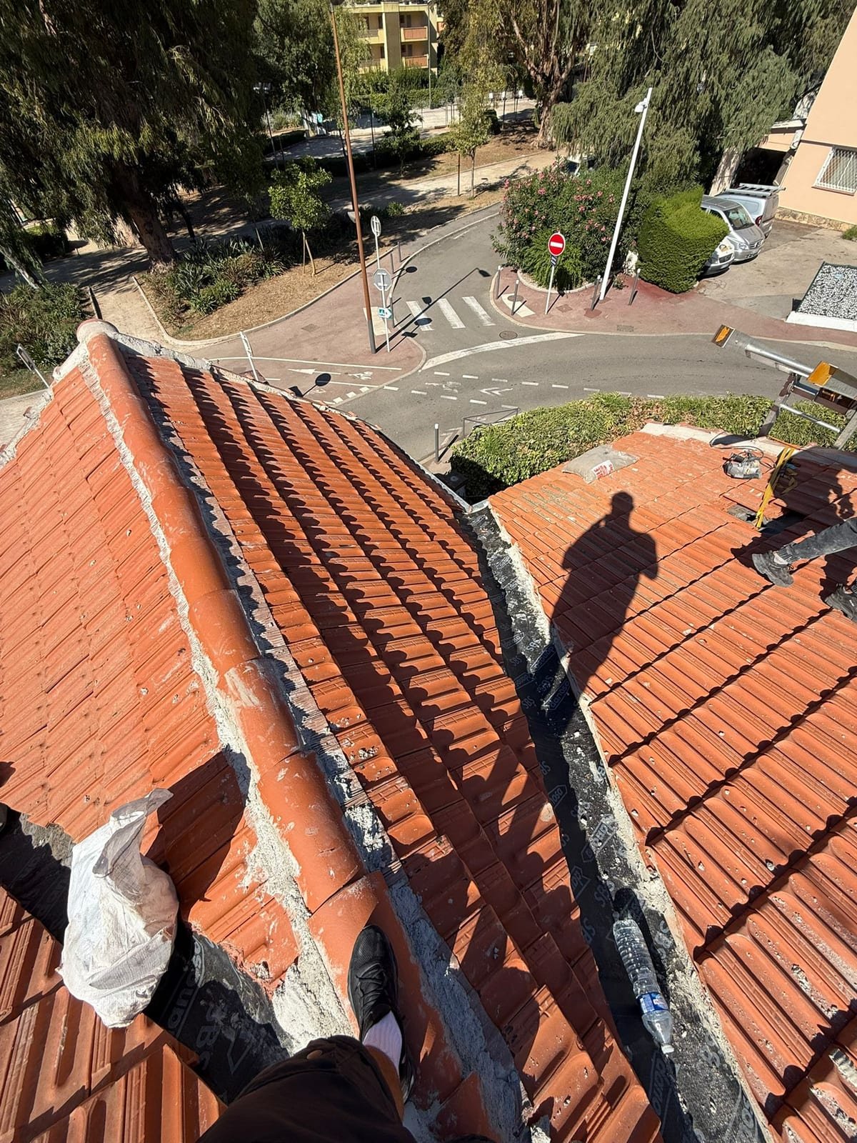 Vue plongeante depuis le faîtage sur deux versants de toiture en tuiles rouges, arêtier maçonné et noue traitée entre les pans