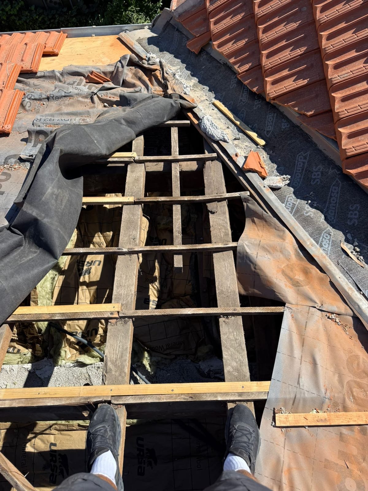 Zone de toiture déposée montrant des liteaux neufs posés à côté de liteaux anciens, isolant en laine minérale visible en dessous