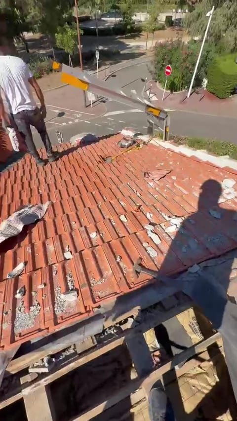 Vue filmée en plongée d'un versant de toiture en tuiles pendant la dépose, un couvreur en déplacement et zone ouverte en partie basse