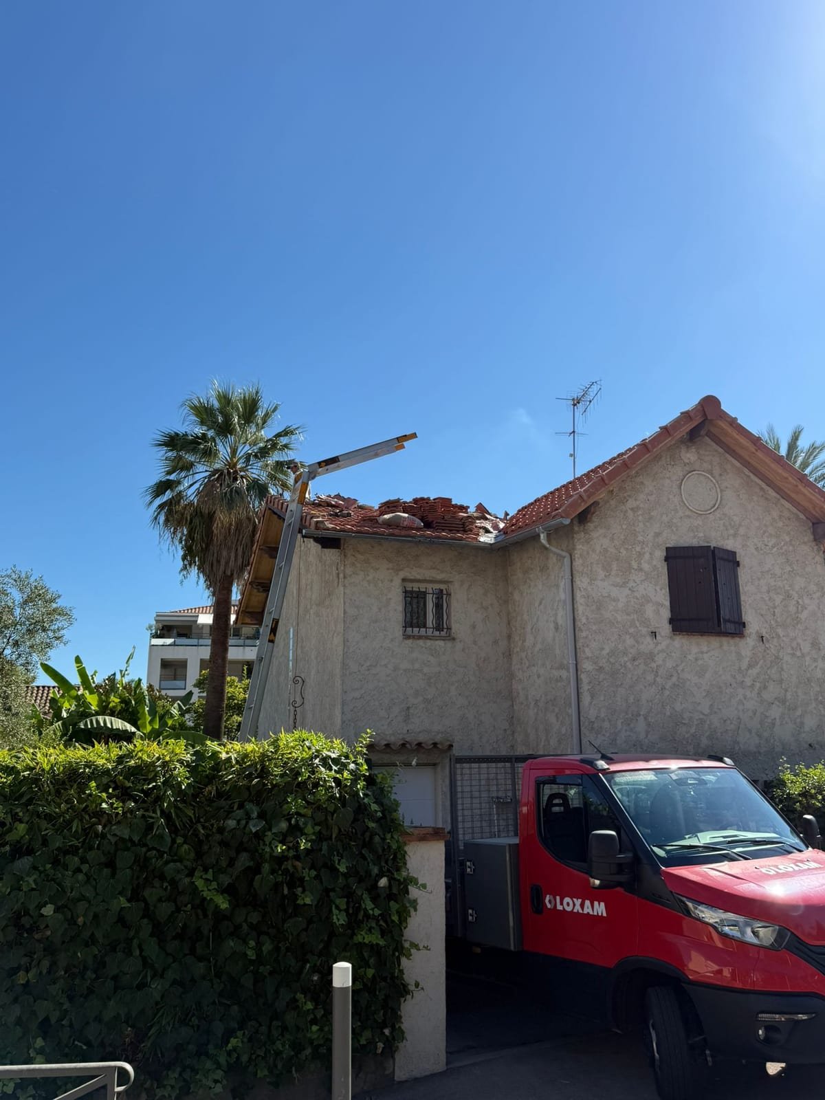Maison à façade enduite vue depuis la rue, toiture en cours d'intervention avec échelle de toit posée sur le versant